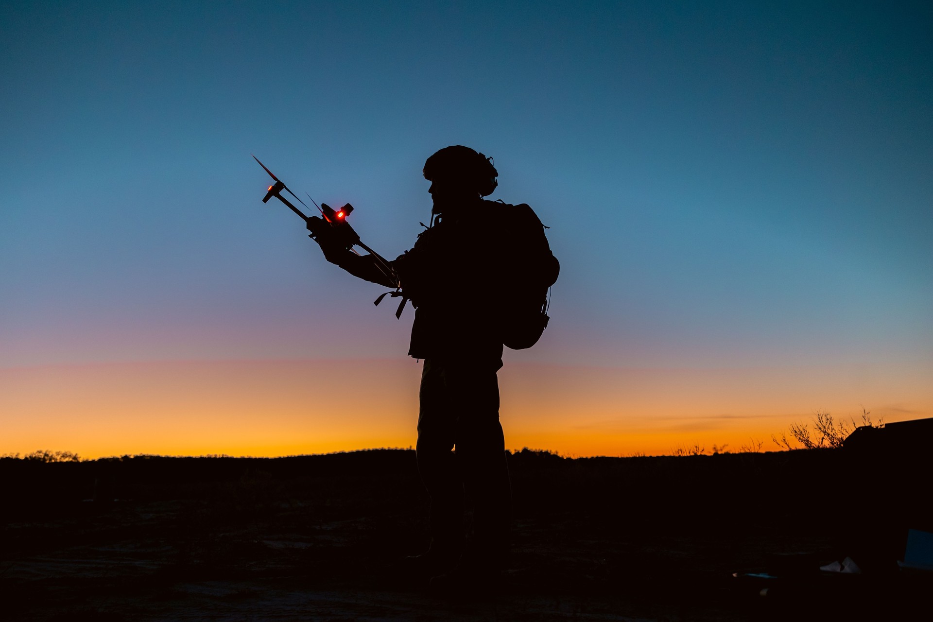 Silhouettes of soldiers are using drone for scouting during military operation against the backdrop of a sunset.